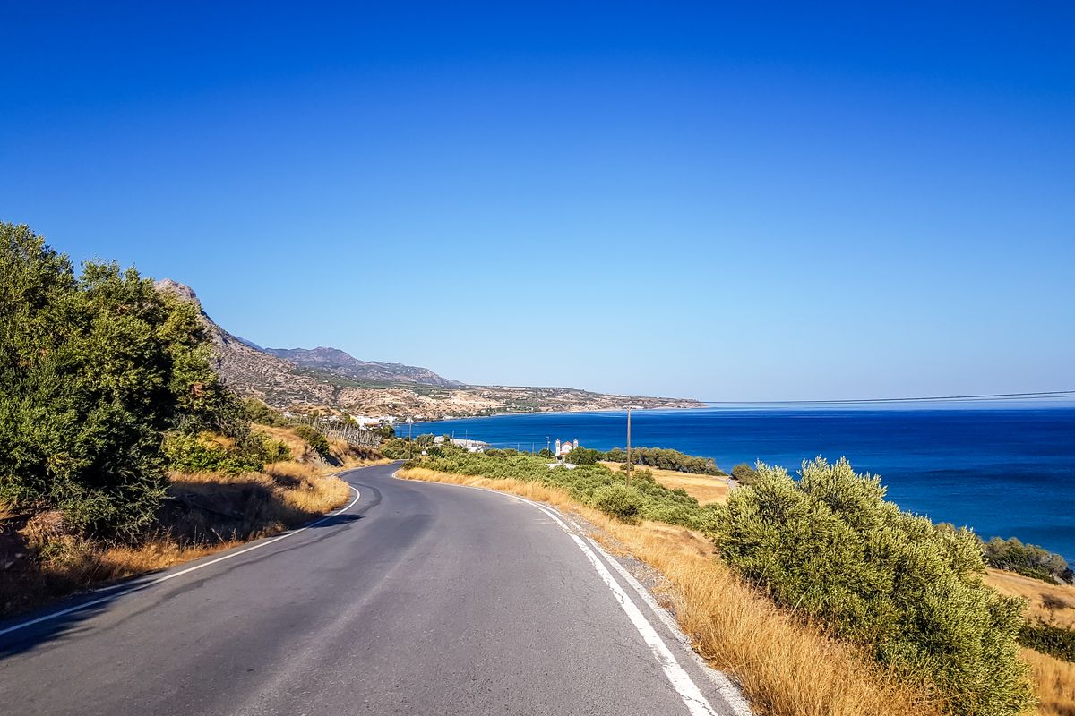 Coastal road descending toward a bay in Crete with dry hills
