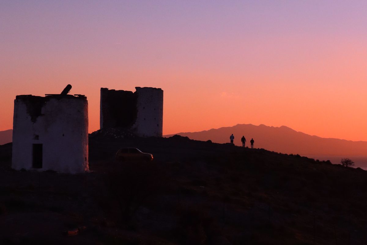 Ruined stone windmill towers on a Greek ridge at dusk
