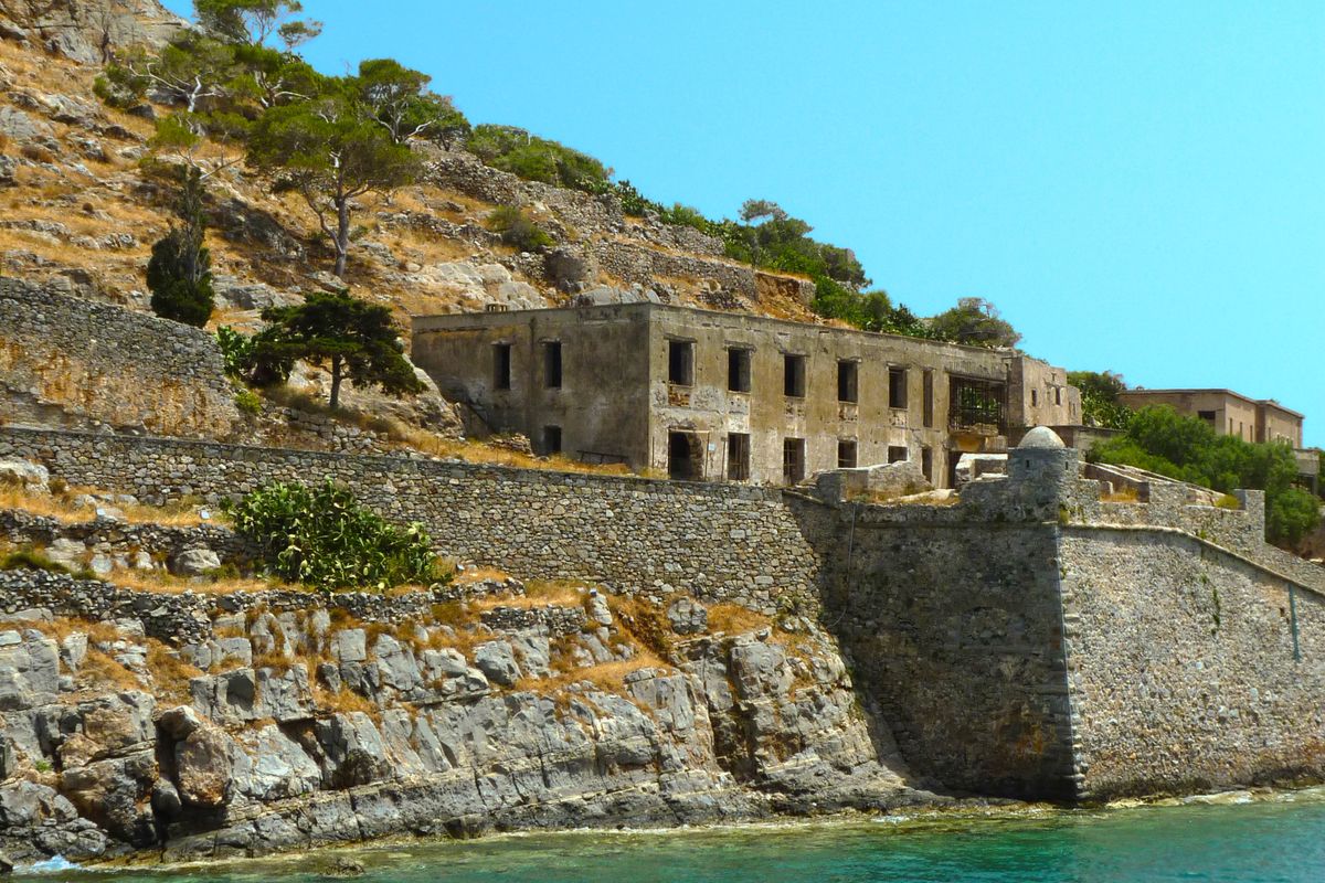 Abandoned stone buildings of the Spinalonga village standing above the fortress sea wall, ruined houses of the former leper colony